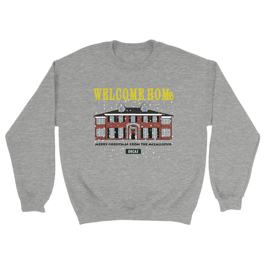 Sweatshirt couleur gris avec une illustration de la maison du film culte de noël, Maman j'ai raté l'avion (home alone) et les textes suivants : en jaune "welcome home" et en noir "merry christmas from the mccallister"