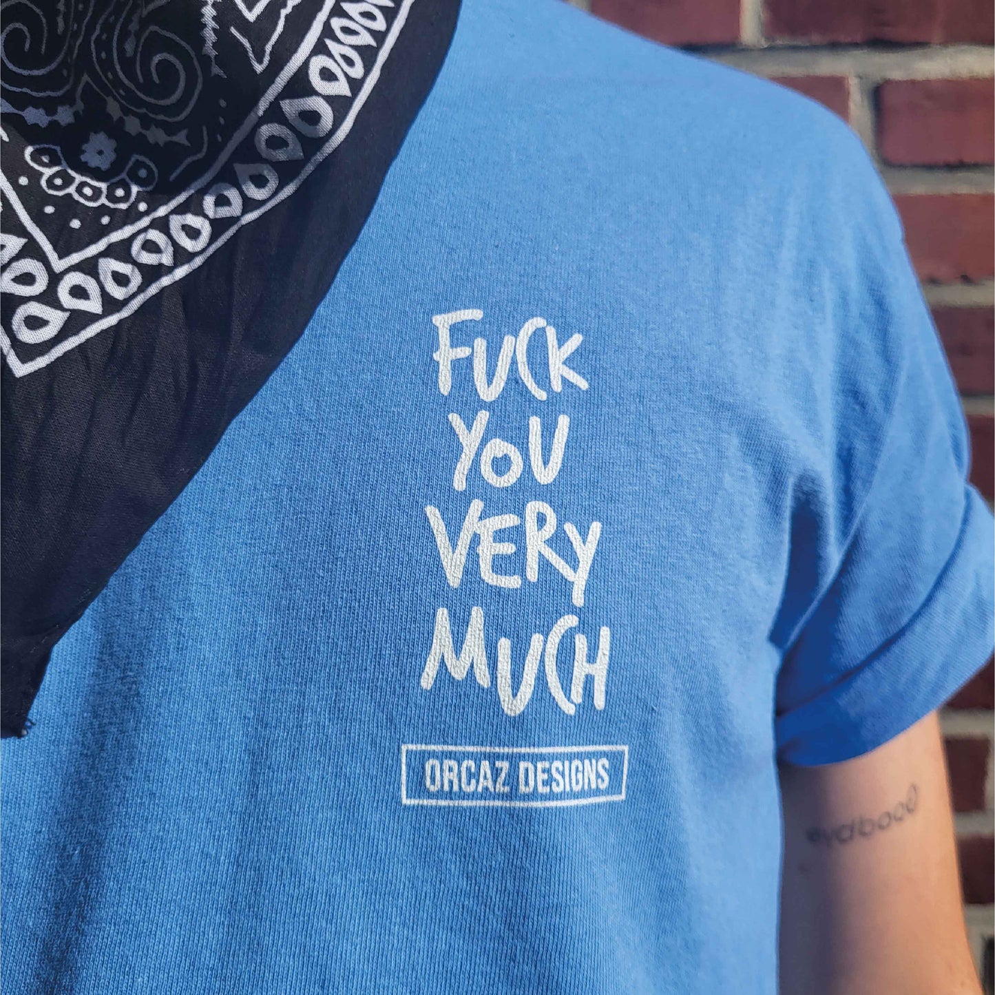 Photo de près d'un tee-shirt bleu ciel où il est écrit "fuck you very much" sur le coeur avec le logo Orcaz Designs