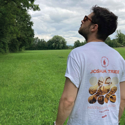 Photographie d'un jeune homme portant un tshirt graphique blanc en coton avec une photo du parc national de joshua tree avec des textes de couleur orange